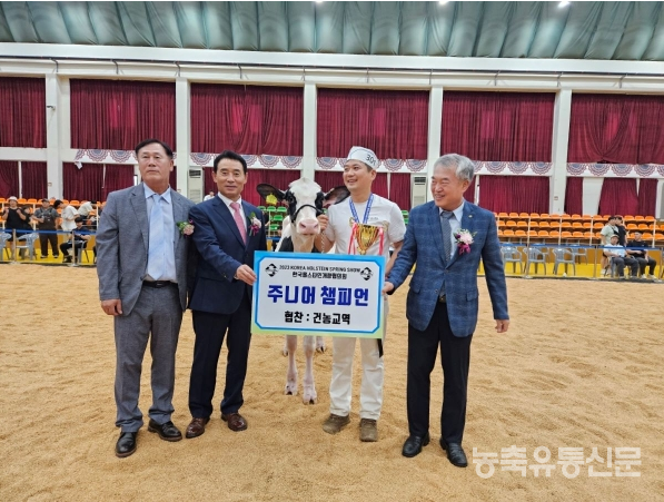 교수님 학생이 젖소를 가운데 두고, 주니어 챔피언 협찬:건농교역 배너를 들고 기념사진을 찍고 있다.