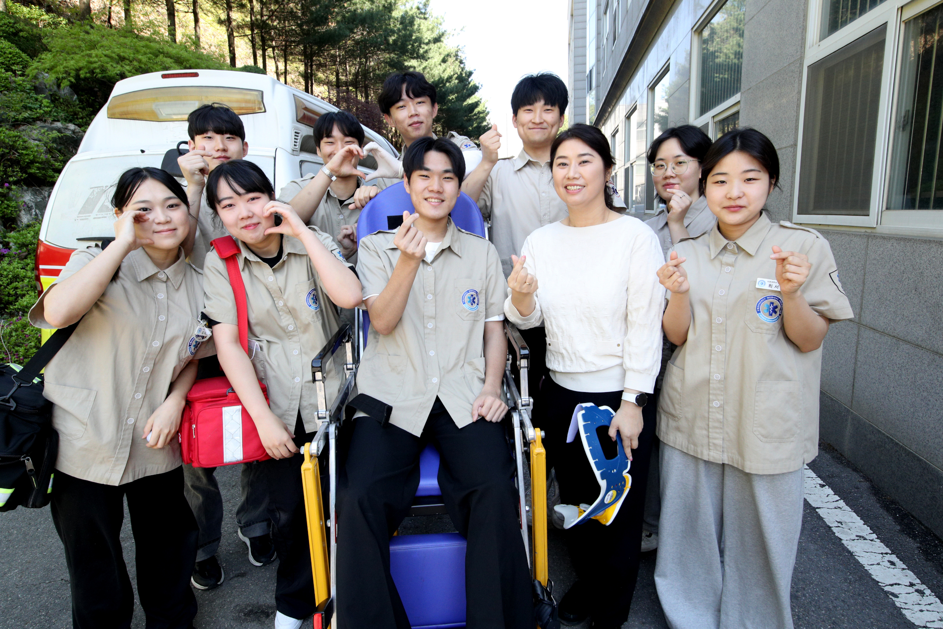 소방차를 배경으로 찍은 응급주조과 학생들의 사진들. 학과 셔츠를 입고 손으로 하트를 그리고 있다. 가운데 사람은 이송 의자에 앉아있고 그 오른쪽에 흰 옷을 입은 교수님이 서있다.