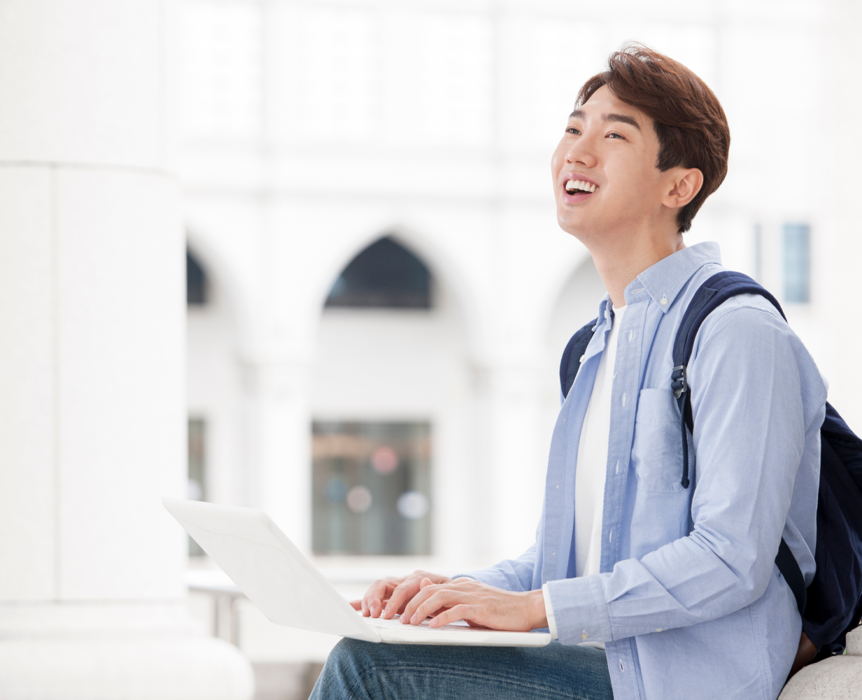 돌 계단에 앉아 노트북을 하면 웃는 남학생의 사진