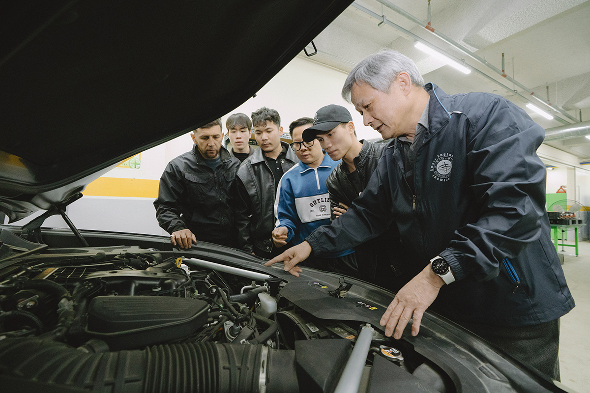 자동차 본네트를 열고 설명하는 교수님과 설명을 듣는 학생들