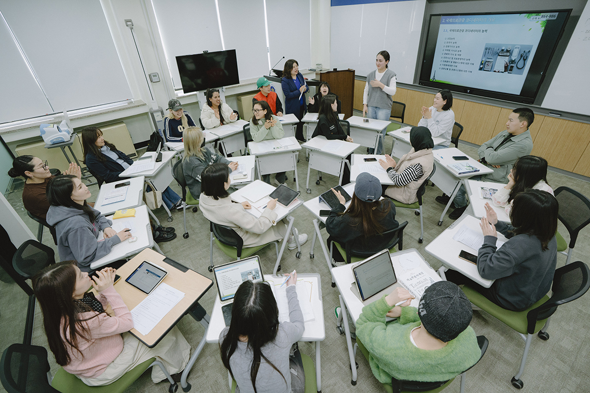 테이블을 둘글게 배치해 앉아있는 학생들과 수업중인 교수님