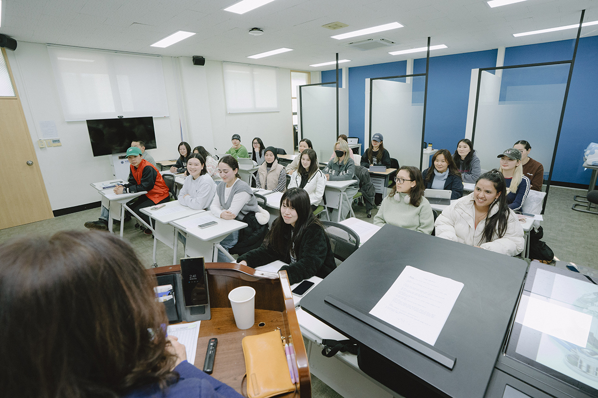 테이블을 둘글게 배치해 앉아있는 학생들과 수업중인 교수님